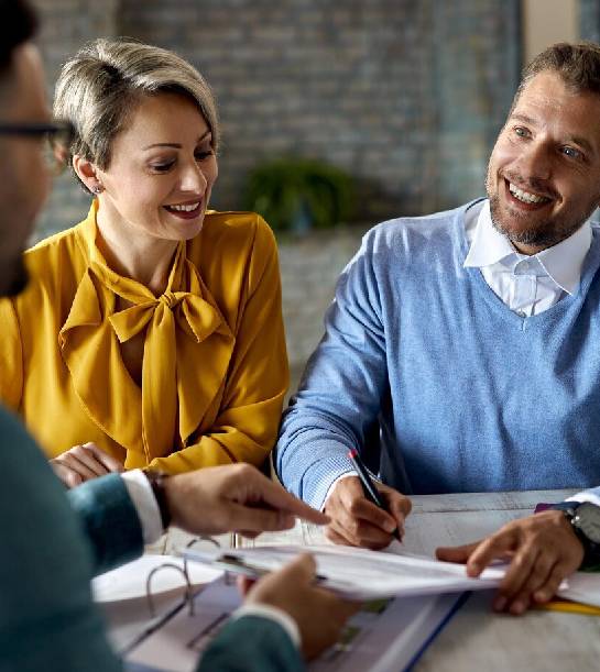 Happy couple signing paperwork while having a meeting with financial advisor in the office<br />